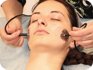 Frau mit geschlossenen Augen während einer Gesichtsbehandlung mit zwei Metallapplikatoren an den Wangen