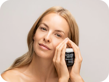 Frau hält ein Kosmetikprodukt an ihre Wange und blickt ruhig in die Kamera